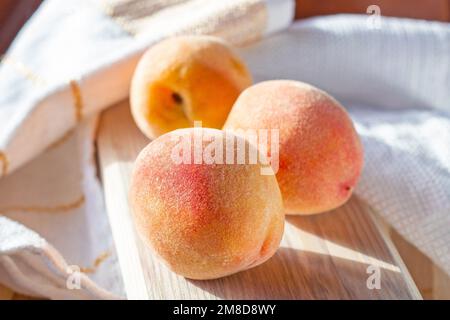 Tre pesche fresche e succose rosse e arancioni sulla tavola di legno nella cucina soleggiata in estate. Foto Stock