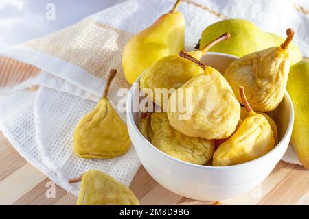 Pere intere essiccate di colore giallo brillante nel recipiente bianco e frutta fresca sullo sfondo di legno primo piano. Foto Stock