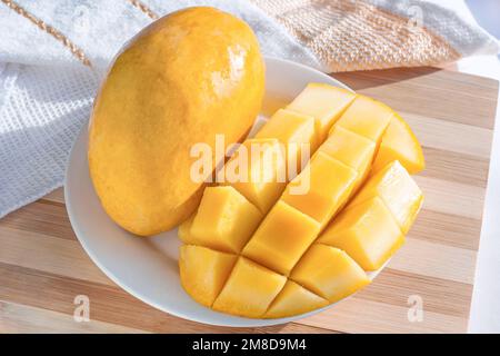 Cubo giallo brillante tagliato mango fresco sul piatto bianco sul tagliere di legno primo piano. Foto Stock