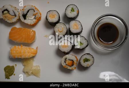 Three types of sushi with soy sauce and wasabi placed on a white plate. Stock Photo