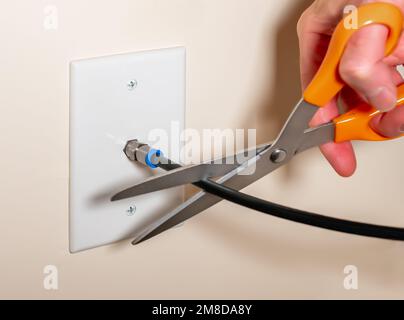 Annullare il servizio TV via cavo tagliando il collegamento del cavo coassiale. Primo piano della mano maschile utilizzando le forbici per disconnettere l'abbonamento televisivo. Foto Stock