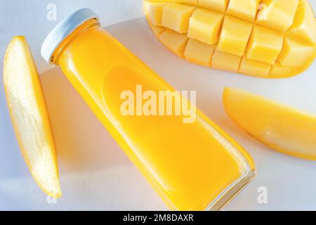 Succo di mango giallo brillante in una bottiglia di vetro con i mango freschi a fette su fondo bianco primo piano. Foto Stock