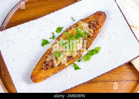 Canoe di piantana mature dolci al forno (Canoas de Platanos Maduros) farcite con carne macinata, formaggio e verdure su un piatto su sfondo di legno vista dall'alto. Foto Stock