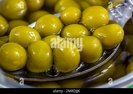 Cucchiaio che tiene i piselli verdi dolci marinati in contenitore di metallo vicino. Foto Stock