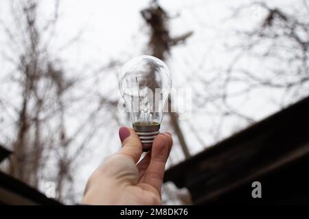 Una lampadina incandescente nelle mani di una ragazza contro il cielo, un vozli a casa, persone senza luce, luce Foto Stock