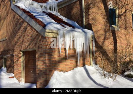 Sciogliendo neve sul tetto creando diga di ghiaccio in grondaia e ghiaccioli che tirano giù sulla grondaia. Foto Stock