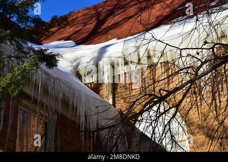 Sciogliendo neve sul tetto creando diga di ghiaccio in grondaia e ghiaccioli che tirano giù sulla grondaia. Foto Stock