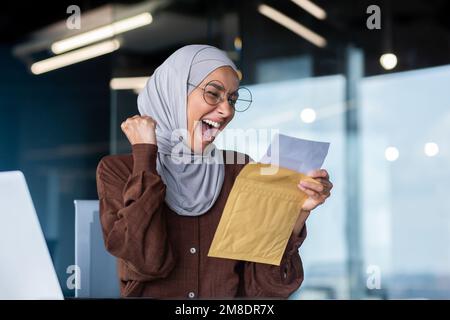 Donna d'affari di successo in hijab celebrare la vittoria e successo successo successo donna musulmana in ufficio con notebook ricevuto buono . Foto Stock