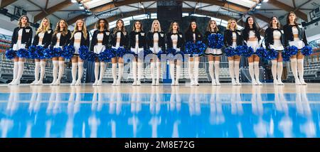 Vista ad angolo basso delle cheerleaders in mini-gonne in piedi in fila con pom-pom. Foto Stock