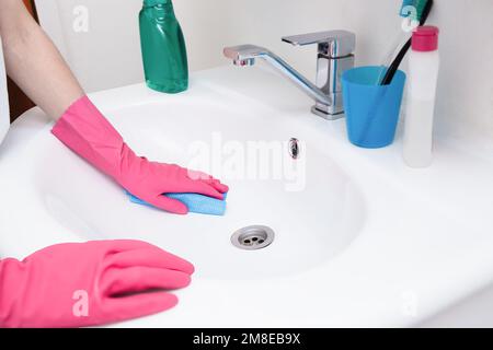 Pulizia della casa in bagno. Donna in guanti rosa che pulisce un lavello bianco con una spugna e spray e detergente. Igiene a casa, pulizia della casa, KE Foto Stock