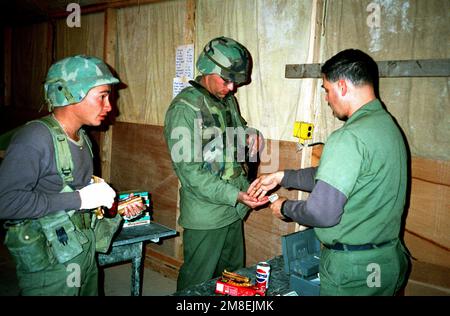 IL MASTER CHIEF PETTY Officer Ricardo Garza restituisce il cambiamento all'ENS. Mark Chenoweth come PICCOLO ufficiale 3rd Classe Todd Metzgar aspetta di pagare per un acquisto in uno scambio in un campo in costruzione nel nord dell'Arabia Saudita durante l'operazione Desert Storm. Gli uomini sono Seabee con Naval Mobile Construction Battalion 5 (NMCB-5). Soggetto operativo/Serie: TEMPESTA DEL DESERTO Paese: Arabia Saudita (SAU) Foto Stock