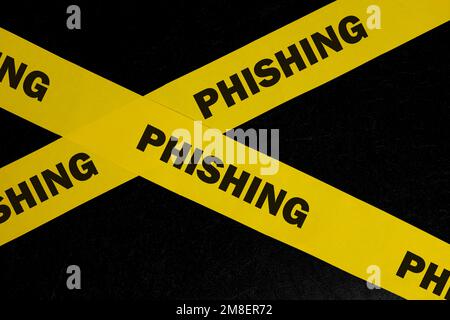 Avviso di phishing, attenzione e avviso. Nastro barricata giallo con phishing parola su sfondo nero scuro. Foto Stock