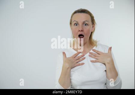 La donna adulta è molto sorpresa, ha aperto la bocca e le ha appoggiate le mani con palmi aperte al petto, come se chiedesse che cosa sono, i suoi occhi sono spalancati, una persona reale semplice, nessun hairstyle, nessun trucco Foto Stock