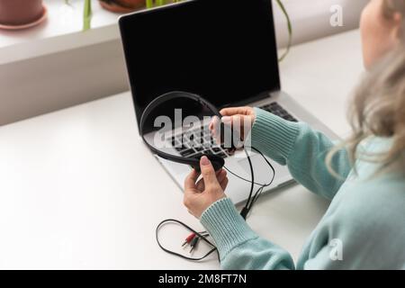 Vista laterale testa scattata sorridente signora freelancer gara mista indossando cuffie, comunicando con il cliente tramite videochiamata al computer. Piacevole millenario Foto Stock