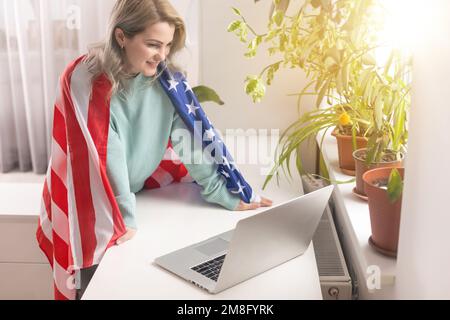 Insegnante positivo in cuffie con microfono che ha una lezione online sul laptop vicino alle bandiere a scuola Foto Stock