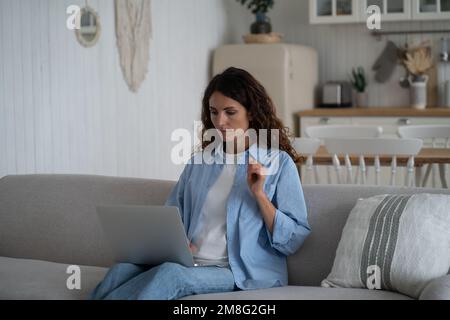 Donna solista pensiva che lavora da casa sul divano, usando un notebook. Concetto di home Office Foto Stock
