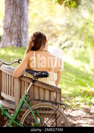 A volte tutti vogliono fuggire. Ripresa da dietro di una giovane donna seduta su una panchina con la bicicletta dietro di lei. Foto Stock