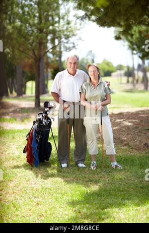 Buon gioco di golf. Ritratto di una coppia matura e felice in piedi insieme sorridendo su un campo da golf. Foto Stock