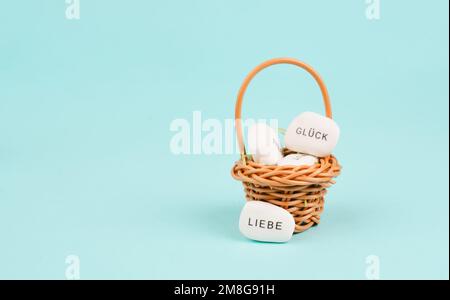 Cestino con ciottoli bianchi, parole come la fortuna e l'amore in piedi in lingua tedesca sulle pietre, regalo con buoni auguri Foto Stock