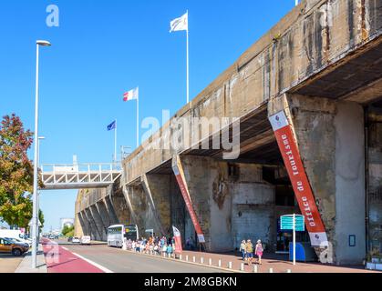 I turisti anziani aspettano un tour guidato del porto di fronte all'ex base sottomarina costruita dall'esercito tedesco durante la seconda guerra mondiale a Saint-Nazaire, Francia Foto Stock