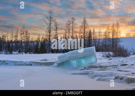 Un blocco di ghiaccio turchese stratificato sulla riva del fiume alla luce del tramonto. Paesaggio invernale serale Foto Stock