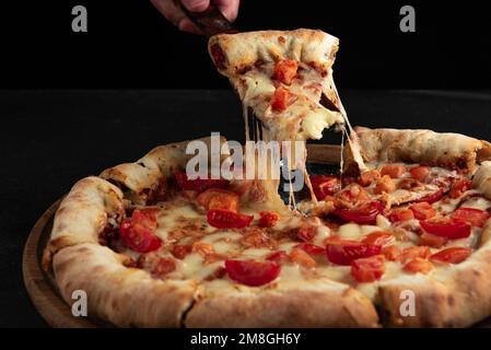 Una fetta di pizza al formaggio indiano su sfondo scuro. Formaggio che raggiunge per una fetta di pizza Foto Stock