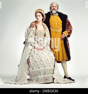 Re, regina e corona con una coppia in studio su uno sfondo grigio durante il periodo rinascimentale o vittoriano. Regalità, storia e vintage con un uomo Foto Stock