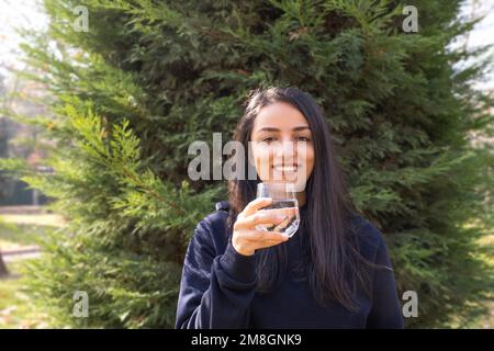 Donna sorridente felice bicchiere d'acqua. Sfondo verde natura. Spazio di copia. Abitudini di vita sane. Consigliare di bere liquidi. Idea di concetto naturale. Foto Stock