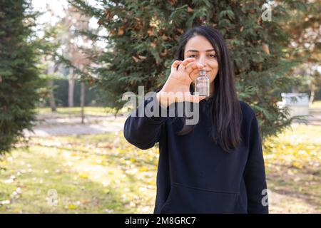 Donna che tiene e mostra vuoto flacone di pillole della medicina. Autunno foresta o parco sfondo. Sorridente bella signora che consiglia i supplementi della vitamina mock in su. Foto Stock