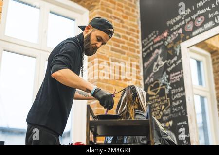 barbuto parrucchiere in abiti neri tintura capelli cliente, salone medio colpo. Foto di alta qualità Foto Stock