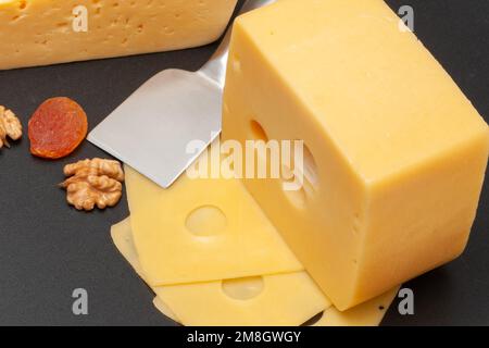 Diversi tipi di formaggio su un pannello di legno decorato con uva, albicocche secche e noci Foto Stock