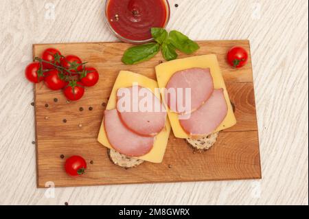 Sandwich con prosciutto e formaggio su un pannello di legno decorato con pomodori ciliegini e basilico Foto Stock