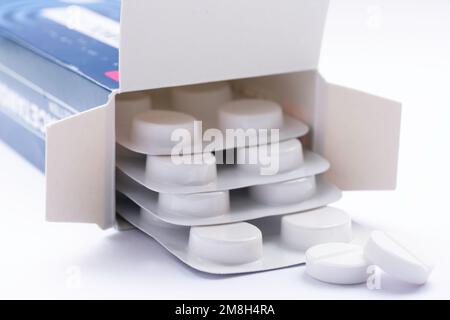 Scatola di cartone aperta con compresse o pillole in blister su sfondo bianco. Concentratevi sui due tablet che si trovano davanti, con una profondità di campo ridotta Foto Stock