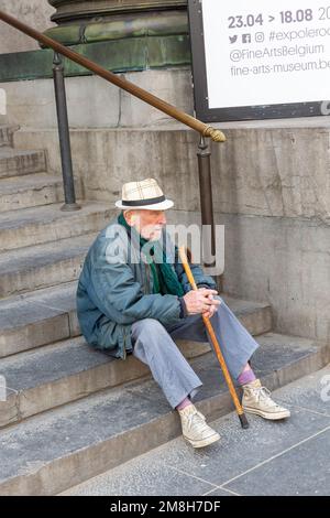 Uomo con un bastone e un cappello di paglia poggiato sui gradini di una scala. Bruxelles. Foto Stock