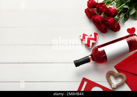Bottiglia di vino, fiori di rosa, busta e cuori su fondo di legno bianco. Festa di San Valentino Foto Stock