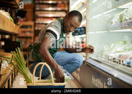 Supermarket worker che controlla la qualità degli alimenti e mette i prodotti scaduti nel cestino Foto Stock