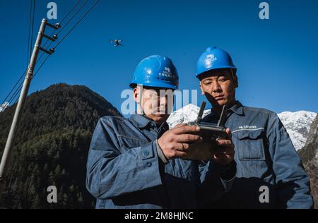 (230114) -- DEQEN, 14 gennaio 2023 (Xinhua) -- Wangden (R) e il suo collega Zhang Jincheng usano un drone per ispezionare le linee di trasmissione di potenza nella contea di Deqen, provincia di Yunnan nella Cina sudoccidentale, 10 gennaio 2023. Wangden, 34 anni, è il direttore associato della filiale Yunnan della centrale elettrica Yanmen della China Southern Power Grid nella contea di Deqen. Nel 2015 fu incaricato di svolgere attività di manutenzione a Yubeng, un villaggio locale situato ai piedi di montagne innevate. In qualità di lavoratore di fornitura di energia da più tempo, l'uomo ha assistito a cambiamenti tremendi nel villaggio. In passato, Yube Foto Stock