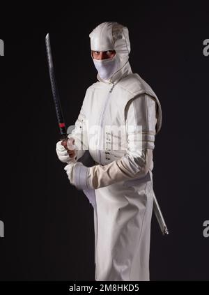 Ninja posa per una foto su uno sfondo nero, un ninja maschio in un kimono bianco. Foto Stock