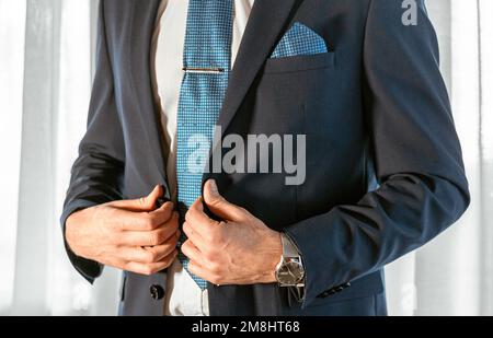 L'uomo in tuxedo blu corregge i bottoni sulla giacca. Dettagli matrimonio. Si può vedere la piazza blu cielo tasca, la clip cravatta e l'orologio sul polso Foto Stock