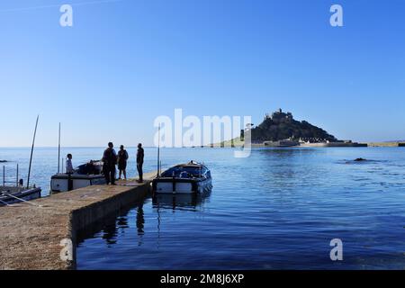 Uomini di traghetto in attesa sulla terraferma per il trasporto dei turisti a St. Monte di Michele in alta marea, Cornovaglia, Regno Unito - John Gollop Foto Stock