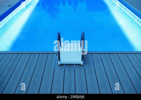 Illuminazione a LED blu piscina residenziale esterna illuminata con una scala di plastica durante le ore serali. Foto Stock