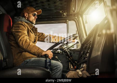 Conducente di veicoli semi professionali al volante di un veicolo classico. Autista commerciale caucasico nel suo 40s. Tema dell'industria dei trasporti. Foto Stock