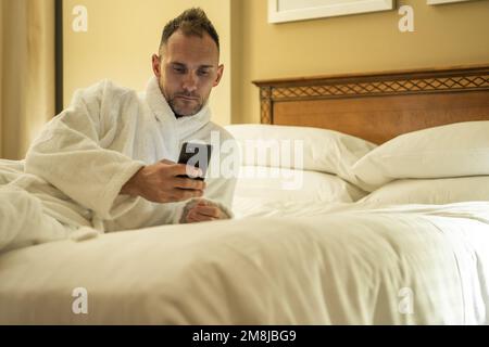 L'uomo caucasico che verifica i suoi profili dei social media prima di andare a dormire all'interno di una camera d'albergo. Foto Stock