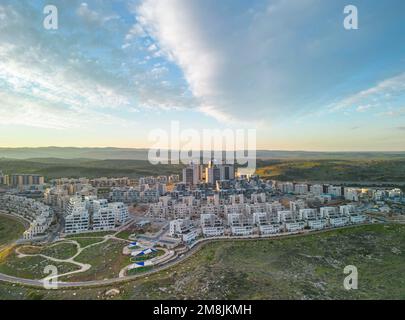 Modiin, Israele, 12 gennaio 2023 costruzione di un edificio residenziale a più piani e di una grande nuova zona residenziale che si affaccia su un parco verde con alberi e un prato vicino a edifici residenziali contro un cielo blu con nuvole bianche. Foto di alta qualità Foto Stock