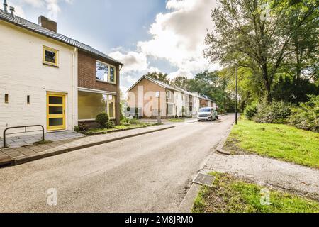 una strada vuota con case sullo sfondo e erba verde su entrambi i lati, c'è una macchina bianca parcheggiata accanto ad essa Foto Stock