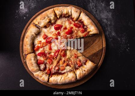 Pizza margarita con pomodori e formaggio su sfondo scuro vista dall'alto. Pizza italiana senza una fetta. Foto Stock