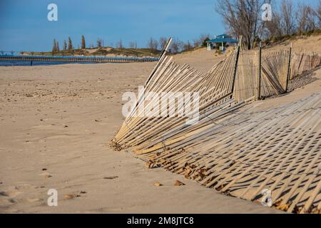 Una recinzione in una duna di sabbia con molte linee diagonali e luce del sole che getta ombre. Foto Stock