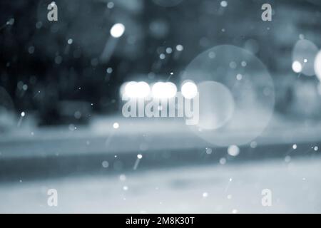 Sfondo sfocato. Auto che guidano su strada in città durante le nevicate nella notte d'inverno. Macchie bokeh sfocate. Illuminazione stradale, lanterne, luce di fari luminosi. Scenario invernale sfondo. Colore blu Foto Stock