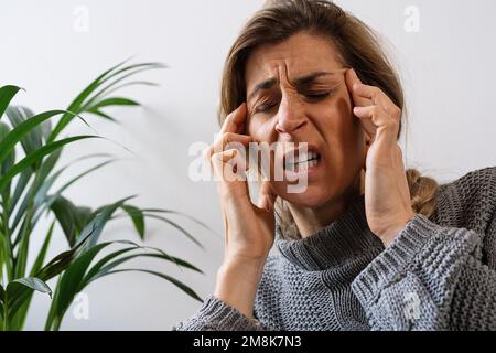 donna seduta sul divano sensazione di forte emicrania cefalea. Concetto di medicina e assistenza sanitaria. Foto Stock