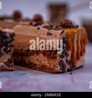 Un primo piano del pezzo di una torta con crema di cioccolato decorata con scaglie di cioccolato e palline su uno sfondo sfocato Foto Stock